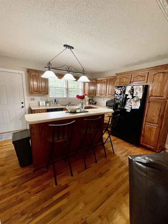 kitchen featuring black fridge with ice dispenser, a textured ceiling, light countertops, a breakfast bar, and a kitchen island