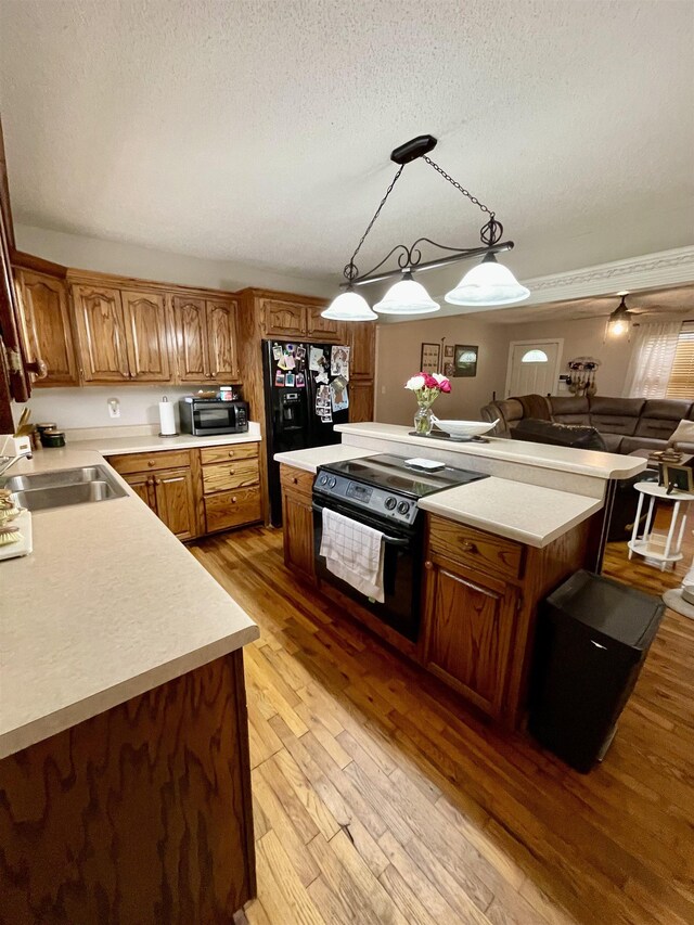 kitchen featuring a sink, black appliances, a textured ceiling, light countertops, and light wood finished floors