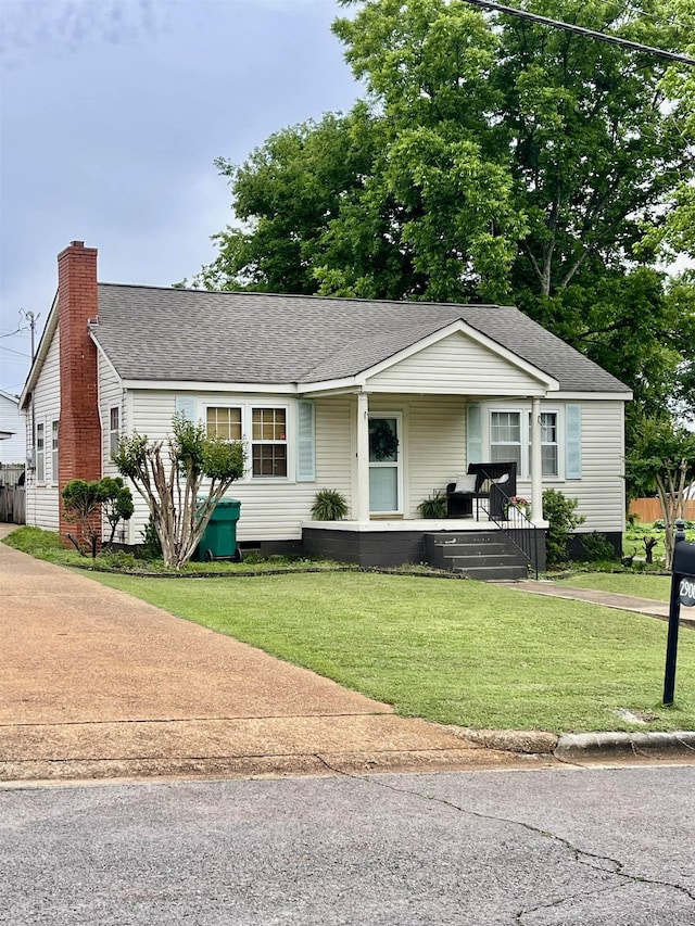 view of front facade with a front lawn, a porch, roof with shingles, and a chimney