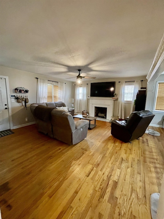 living area featuring a fireplace, light wood-type flooring, ceiling fan, and baseboards