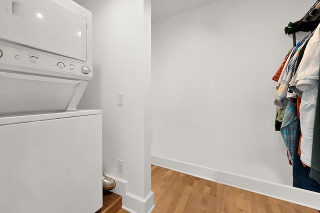 clothes washing area with stacked washer and dryer, light wood finished floors, and baseboards