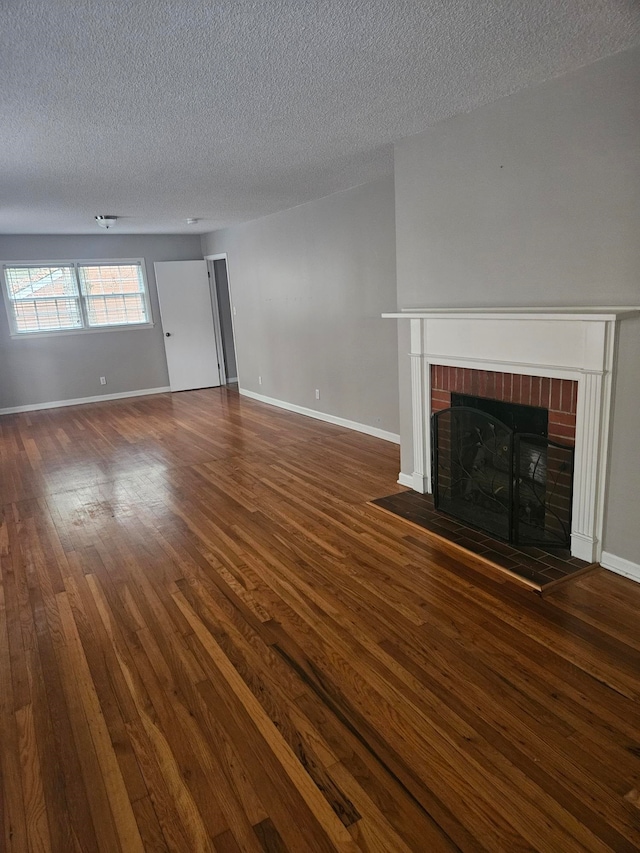 unfurnished living room featuring dark hardwood / wood-style flooring, a textured ceiling, and a brick fireplace