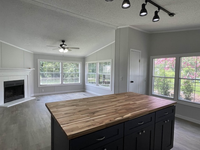 kitchen featuring wood counters, ornamental molding, ceiling fan, a tile fireplace, and a kitchen island