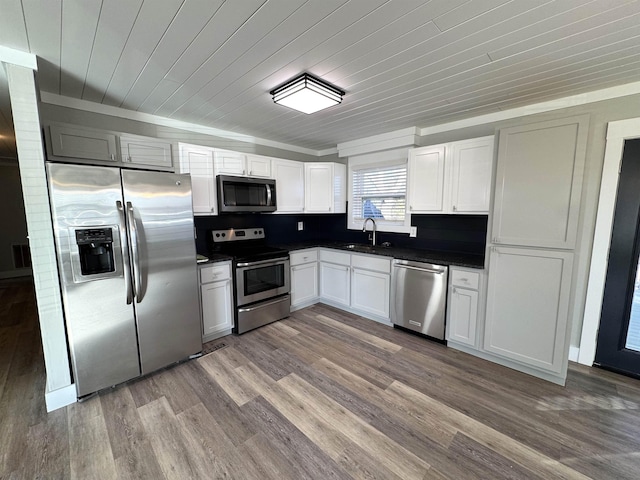 kitchen featuring appliances with stainless steel finishes, white cabinetry, wood-type flooring, sink, and decorative backsplash