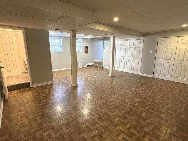 basement featuring dark parquet flooring and a paneled ceiling