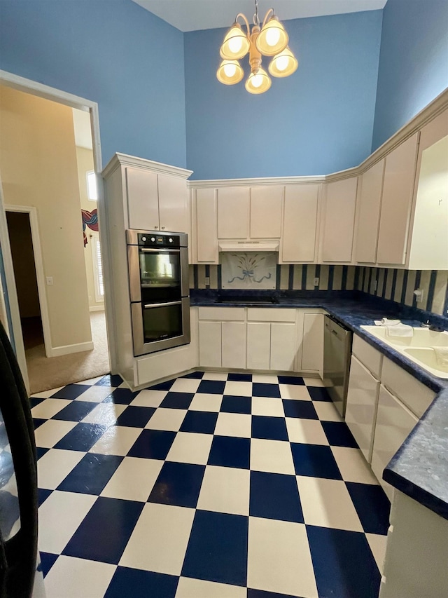  - kitchen featuring stainless steel appliances, a towering ceiling, light floors, a chandelier, and dark countertops