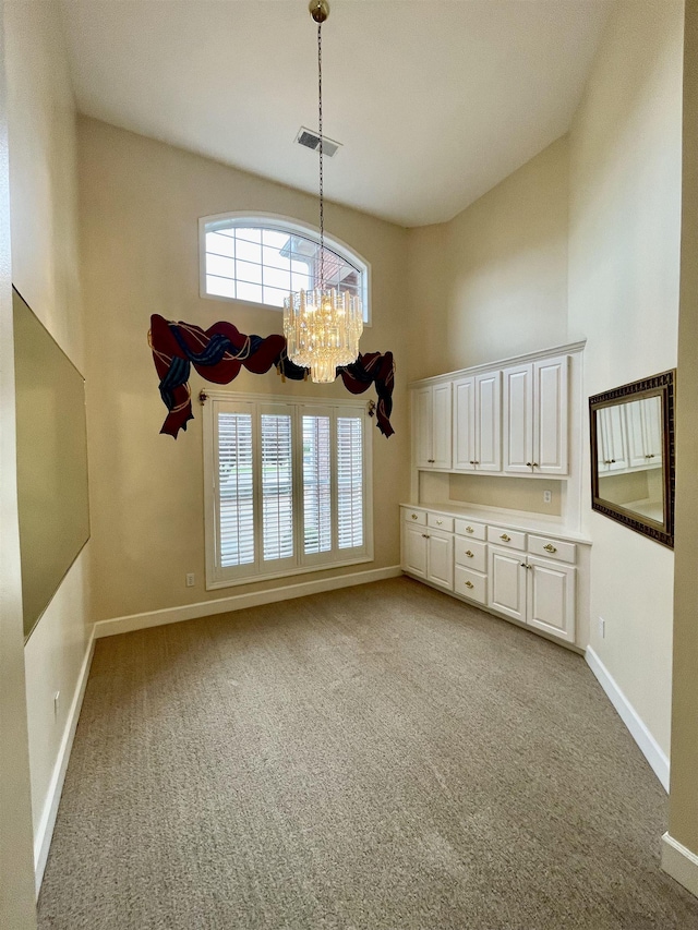  - unfurnished dining area with a high ceiling, a chandelier, and light carpet