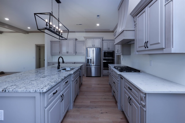 kitchen with gray cabinetry, sink, stainless steel appliances, premium range hood, and an island with sink