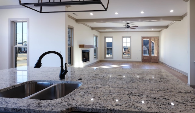 kitchen with sink, ceiling fan, light wood-type flooring, beamed ceiling, and stone countertops