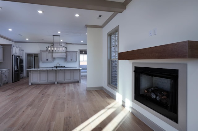 kitchen with light hardwood / wood-style floors, pendant lighting, stainless steel fridge with ice dispenser, gray cabinets, and an island with sink