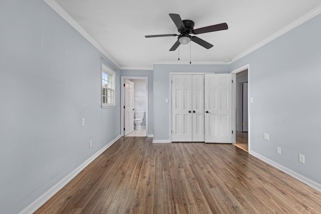  - unfurnished bedroom with ornamental molding, baseboards, wood finished floors, ensuite bathroom, and a closet