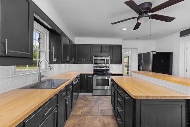  - kitchen with butcher block counters, appliances with stainless steel finishes, a sink, dark cabinets, and backsplash