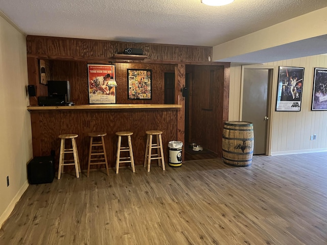  - indoor dry bar featuring wooden walls, wood finished floors, baseboards, and a textured ceiling