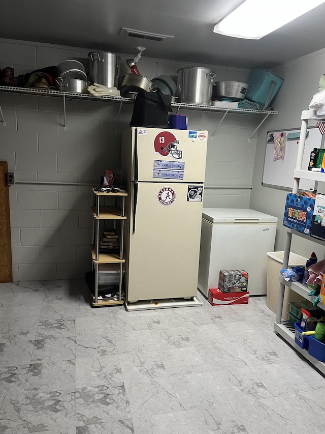  - basement featuring freestanding refrigerator, white fridge, marble look tile flooring, and concrete block wall