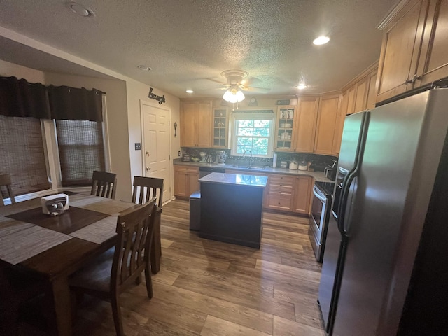  - kitchen featuring stainless steel appliances, a textured ceiling, a kitchen island, ceiling fan, and wood finished floors