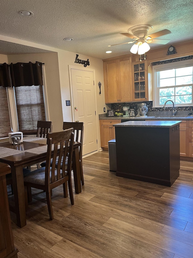  - kitchen featuring a center island, a textured ceiling, dark wood-type flooring, glass insert cabinets, and backsplash