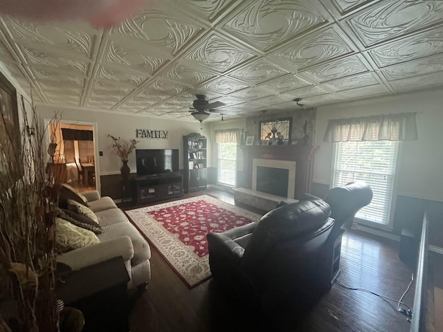  - living room with an ornate ceiling, a ceiling fan, a fireplace with raised hearth, baseboards, and wood finished floors