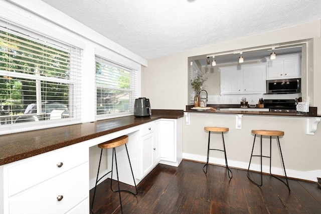  - kitchen with a kitchen breakfast bar, white cabinetry, stainless steel microwave, dark wood finished floors, and range