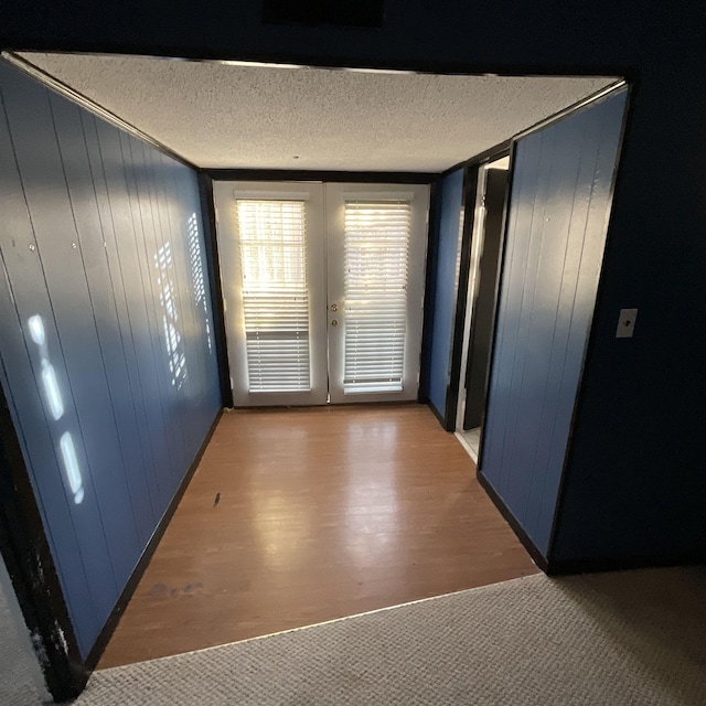 interior space featuring french doors, a textured ceiling, and wood walls