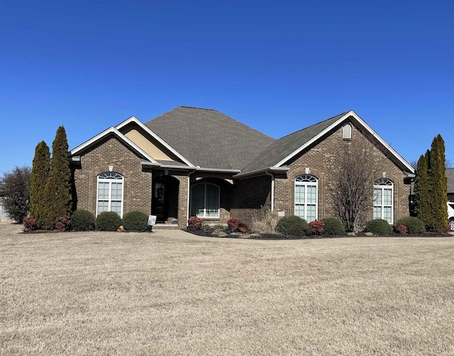 view of front of house featuring a shingled roof, a front yard, and brick siding