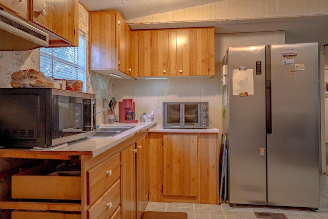 kitchen featuring a textured ceiling, vaulted ceiling, and stainless steel refrigerator