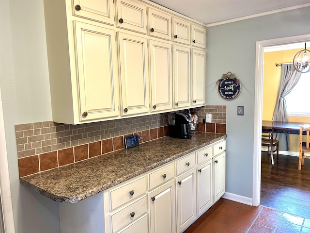 kitchen with backsplash, baseboards, dark tile patterned floors, dark stone countertops, and cream cabinets