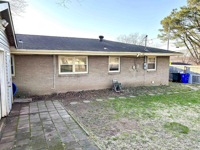 back of house featuring fence, a yard, a shingled roof, brick siding, and a patio area