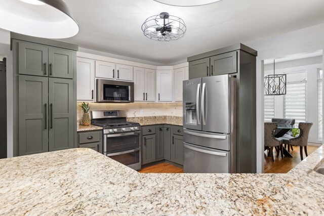 kitchen featuring gray cabinetry, decorative light fixtures, stainless steel appliances, and light wood-type flooring