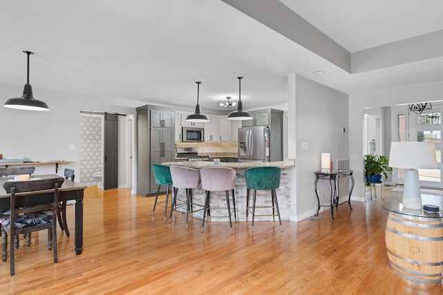 kitchen featuring gray cabinets, appliances with stainless steel finishes, light hardwood / wood-style floors, kitchen peninsula, and a barn door