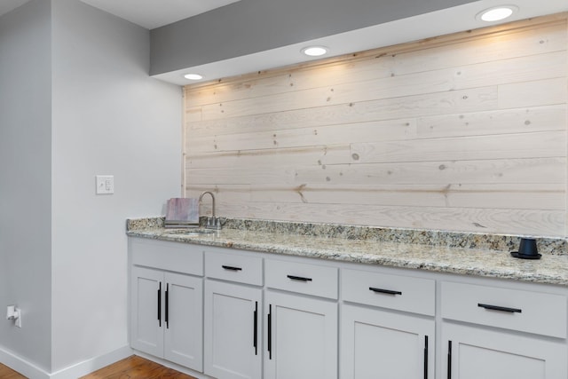 bar with sink, light hardwood / wood-style flooring, and light stone countertops