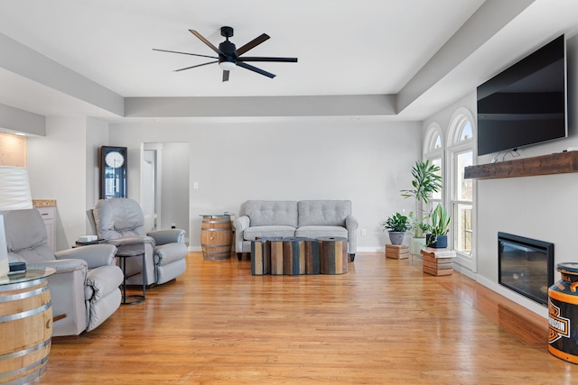 living room featuring ceiling fan, light wood-type flooring, and a tray ceiling