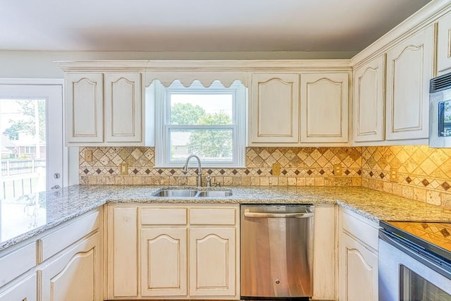 kitchen with tasteful backsplash, light stone counters, stainless steel appliances, sink, and cream cabinets