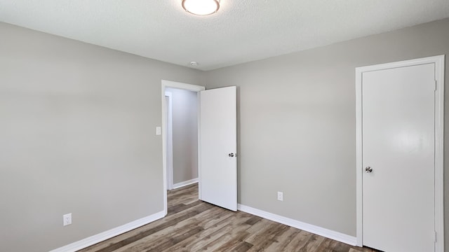 unfurnished bedroom with baseboards, a textured ceiling, and wood finished floors