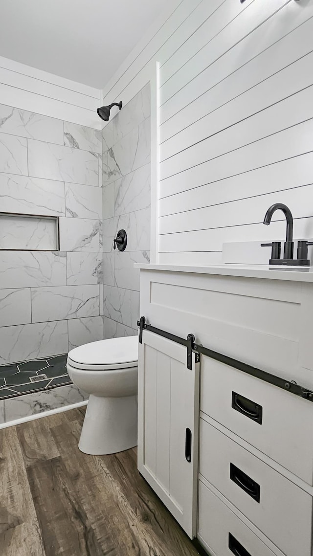 full bath with toilet, tiled shower, vanity, and wood finished floors