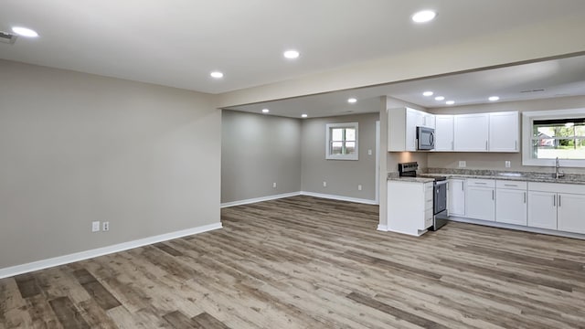 kitchen with baseboards, a sink, open floor plan, stainless steel electric stove, and light wood finished floors