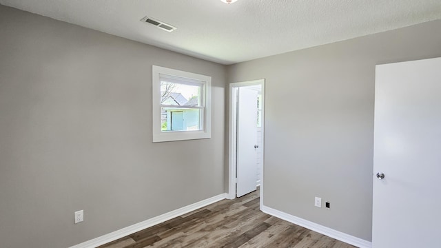 empty room featuring visible vents, baseboards, wood finished floors, and a textured ceiling