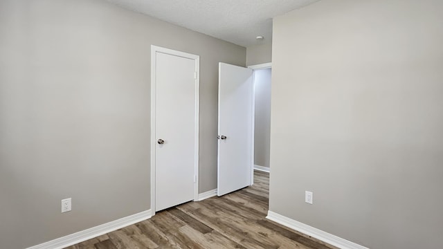 unfurnished bedroom featuring a textured ceiling, wood finished floors, and baseboards