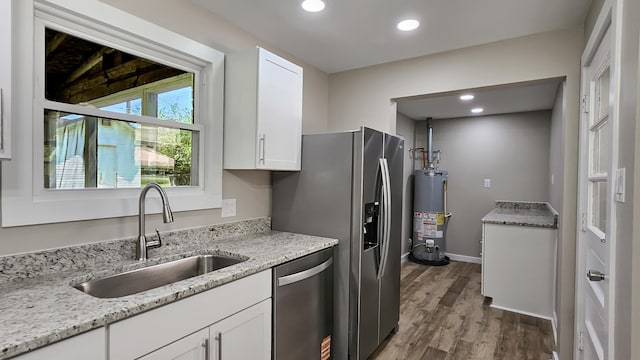 kitchen featuring white cabinets, a sink, wood finished floors, stainless steel appliances, and gas water heater