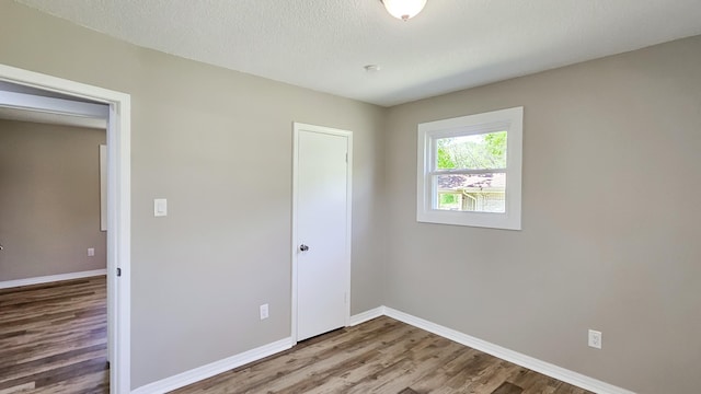 unfurnished bedroom with a textured ceiling, wood finished floors, baseboards, and a closet