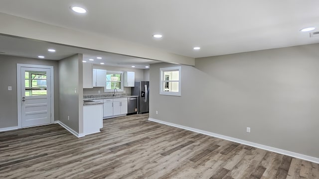 kitchen featuring white cabinets, wood finished floors, a sink, stainless steel appliances, and baseboards
