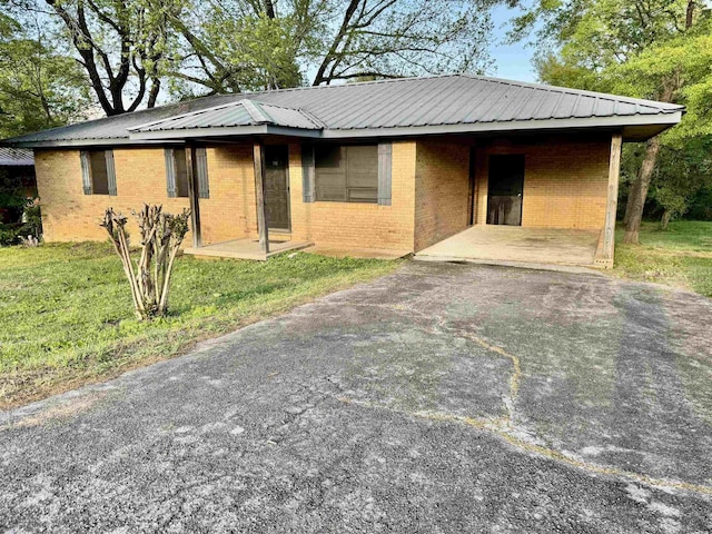 ranch-style home with driveway, brick siding, a front yard, and metal roof