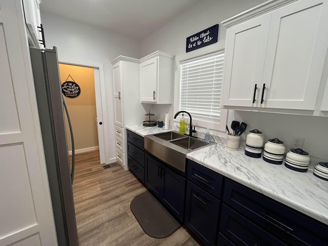 kitchen with stainless steel fridge, sink, light hardwood / wood-style flooring, and white cabinets