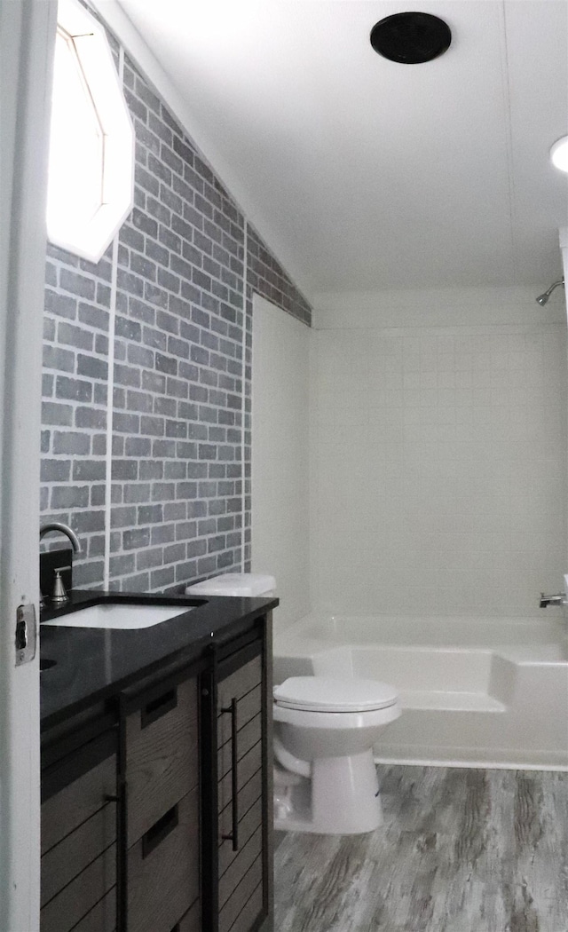 bathroom featuring brick wall, wood-type flooring, toilet, and vaulted ceiling