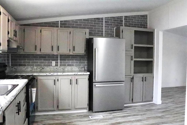 kitchen with extractor fan, range, vaulted ceiling, light wood-type flooring, and stainless steel fridge