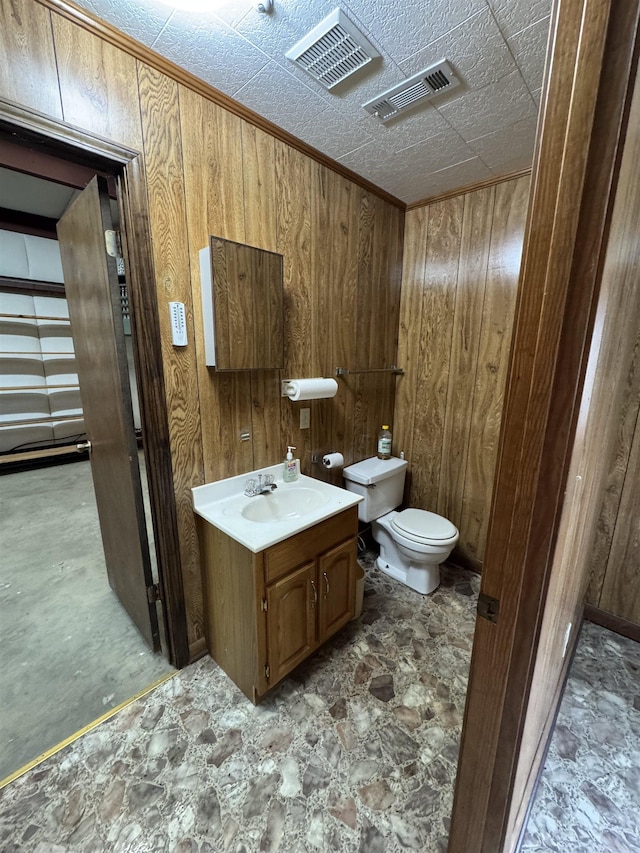 bathroom featuring vanity, wood walls, and toilet