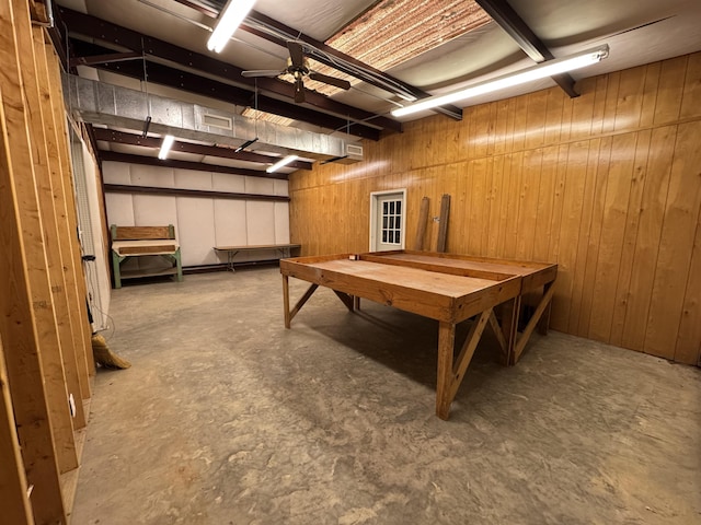 rec room featuring ceiling fan, wood walls, and concrete flooring