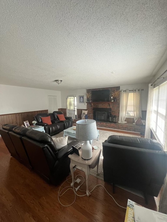  - living room featuring a textured ceiling, wainscoting, healthy amount of natural light, wood finished floors, and a brick fireplace