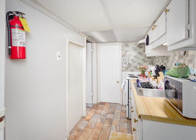  - kitchen featuring white cabinets, white range with electric cooktop, light countertops, tasteful backsplash, and exhaust hood