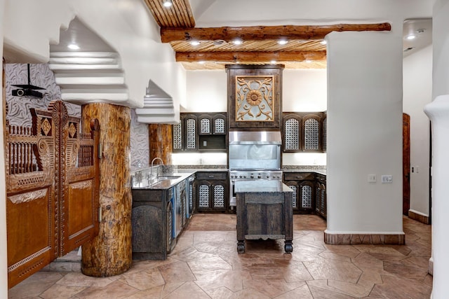 kitchen featuring beamed ceiling, stone finish floor, a sink, a kitchen island, and dark stone counters