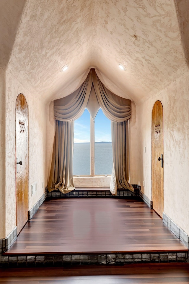 unfurnished dining area featuring visible vents, wood finished floors, baseboards, vaulted ceiling, and a textured wall